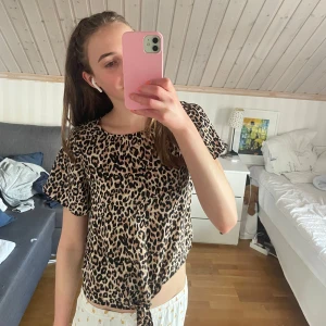 Leopardmönstrad knytblus - Säljer en snygg blus med leopardmönster i beige och svart. Toppen har korta ärmar och en knytning framtill som ger en chill vibe. Perfekt för dig som vill sticka ut lite extra. Passar till både jeans och kjol.