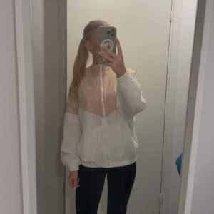 Nike vindjacka i rosa och vitt - Nike vindjacka i rosa och vit-design (mer rosa än vad som syns på bild). Jackan har hel dragkedja framtill och elastiska muddar. Lätt och luftig med klassisk Nike-logga på bröstet. Storlek S. Endast provad, aldrig använd! 