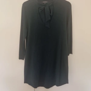 Mörkgrön klänning med rosett - Mörkgrön klänning från Ilse Jacobsen med trekvartsärm och snygg rosettdetalj vid halsen. Rak passform och mjukt material som känns skönt mot huden. Perfekt för dig som gillar stilrena och enkla plagg med en twist.