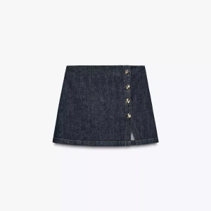 Mörkblå jeanskjol med knappar - Snygg mörkblå jeanskjol/shorts i kort modell med dekorativa knappar längs sidan. Kjolen har en lätt A-linjeform och är tillverkad i klassiskt denimtyg. Perfekt för dig som gillar en stilren och trendig look.