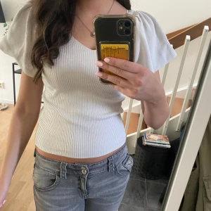 Vit ribbad topp med puffärm - Säljer en vit ribbad topp med v-ringning och korta puffärmar. Toppen är figurnära och har en croppad passform som sitter snyggt på kroppen. Perfekt för både finare tillfällen men även vardag💞