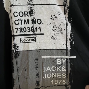 Svart t-shirt Jack & Jones L - Svart t-shirt från Jack & Jones med stor grafisk print i vitt och grått på framsidan. Modellen är klassisk med rund hals och korta ärmar. Tillverkad i 100% bomull för en skön och avslappnad känsla. Perfekt för dig som gillar streetstyle och tydliga tryck.