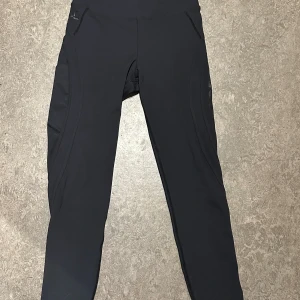 Svarta träningsbyxor från Better Bodies - Svarta träningsbyxor från Better Bodies med hög midja och tight passform. Tillverkade i ett stretchigt syntetmaterial som sitter skönt och följsamt. Perfekta för träning och gym, med diskret logga på linningen. Jag tycker även om att de finns en ficka för din telefon vid benet med! Säljer för 80kr