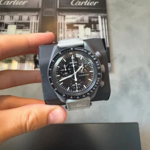 Omega x Swatch Speedmaster MoonSwatch - Omega x Swatch Speedmaster MoonSwatch Mission to Mercury med svart urtavla, grå boett och grått textilband. Klockan har kronograf, tachymeter och tydliga vita visare. Levereras med originalbox och kvitto. En riktigt snygg och ikonisk modell för dig som gillar stilrena accessoarer.