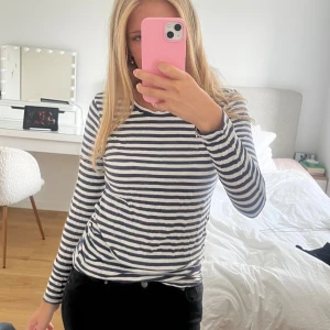 Randig långärmad tröja i bomull - Säljer en klassisk långärmad tröja med marinblå och vita horisontella ränder. Tröjan har rund halsringning och är gjord i mjuk bomull. Perfekt till jeans eller kjol för en chill och stilren look.