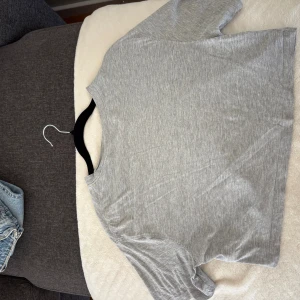 Grå croppad t-shirt - En enkel och stilren grå t-shirt med korta ärmar och croppad passform. Perfekt till jeans eller shorts för en avslappnad look. Mjuk och skön i bomullsmaterial.