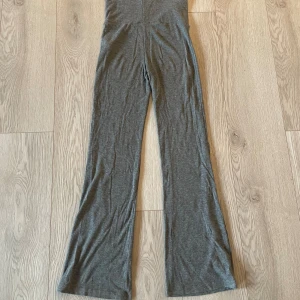 Grå mjukisbyxor från Gina Tricot - Grå mjukisbyxor från Gina Tricot med utsvängda ben och bred, vikbar midja. Byxorna är i mjukt och stretchigt material, perfekta för en chill och avslappnad stil. Passar dig som gillar bekväma och trendiga byxor. Byxorna är lätt ribbade. 