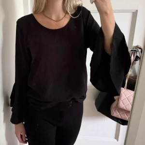 Svart blus med vida ärmar - Säljer en svart blus med rund halsringning och långa, vida trumpetärmar. Blusen har en enkel och stilren design som passar perfekt till många olika outfits. Materialet känns lätt och luftigt. Prislappen kvar.
