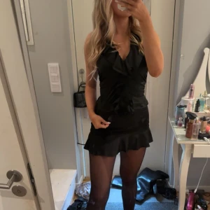 Svart kort volangtopp - Säljer en svart topp med volangdetaljer och v-ringad hals. är ärmlös och har en figurnära passform med snygg volangkant längst ner. Perfekt för dig som gillar en stilren look med lyx, använd 1-2ggr💕 säljer även kjolen på bilden