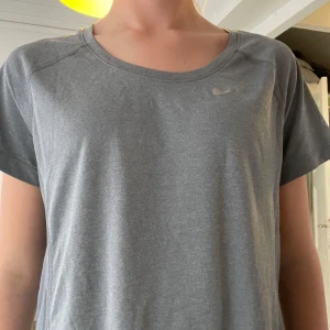Grå Nike Dri-Fit t-shirt - Säljer en grå Nike Dri-Fit t-shirt med rund hals och korta ärmar. Perfekt för löpning eller träning, tillverkad i ett lätt och ventilerande syntetmaterial. Diskret Nike-logga på bröstet och meshpaneler på ryggen för extra andningsförmåga. Det står att den är i storlek large men passar perfekt på mig som brukar använda xs. 