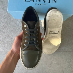  Lanvin skor  - Snygga bruna sneakers från Lanvin med ovandel i mocka och tåparti i glansigt material. Skorna har grå snörning och vit sula. Perfekta för dig som gillar stilrena och exklusiva sneakers. Storlek Uk 7 - 41 sitter som 42. Nypris 4000kr