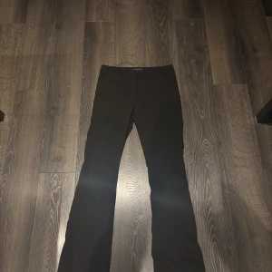 Svarta kostymbyxor med utsvängda ben  - Snygga svarta kostymbyxor med utsvängda ben och klassisk passform. Byxorna har diskreta fickor och stängs med knapp och dragkedja. Perfekta för en clean och stilren look. Materialet känns mjukt och följsamt.nyköpta så aldrig använda men dom passa inte mig så säljer för de. 