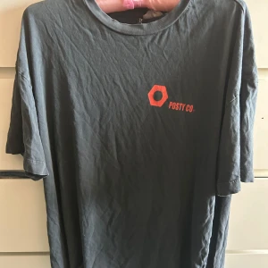 Svart Post Malone t-shirt med tryck - Cool svart t-shirt från Posty Co med röd logga framtill och stort grafiskt tryck på ryggen. T-shirten har rund hals, korta ärmar och är gjord i mjuk bomull. Passformen är loose och trycket har en edgy vibe med text och motiv i rött.