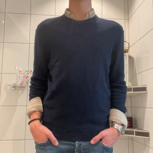 stickad tröja  - En stilren mörkblå stickad tröja i ull med rund halsringning och lång ärm. Perfekt att bära över en skjorta för en clean och klassisk look. Passformen är normal och tröjan har ribbade muddar vid ärmslut och nederkant. Från zara i storlek M. 