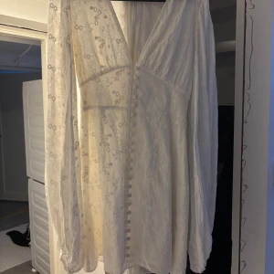 Vit kort klänning från Adoore - Säljer en vit kort klänning från Adoore med v-ringning och långa puffärmar. Säljer då jag beställde fel storlek. Klänningen har broderade blommor, knappar framtill och en lätt transparent känsla. Perfekt för sommarens alla tillfällen, superfin passform och snygga detaljer. Ny pris är 1495kr!