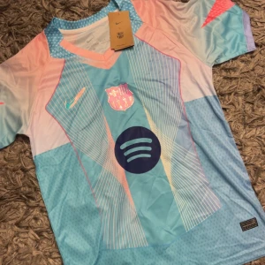 Barcelona Lamine Yamal #10 Nike tröja - Snygg Barcelona fotbollströja med Lamine Yamal och nummer 10 på ryggen. Tröjan har coolt grafiskt mönster i ljusblått, rosa och vitt, med Nike-logga och Spotify sponsor på bröstet. Tillverkad i lätt och ventilerande polyester, perfekt för match eller träning.