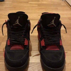 Nike Air Jordan 4 Black/Red - Säljer ett par äkta Nike Air Jordan 4 i svart och rött (red thunder) med klassisk Jumpman-logga på plösen och hälen. Skorna har meshpaneler, snörning och detaljer i rött på sidorna och sulan. Ovandelen är i mocka och de har en chunky siluett som sticker ut. Fick de som present från usa och vill sälja de 
