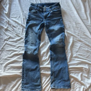Blå bootcut jeans från H&M, stl 164 - Snygga blå bootcut jeans från H&M i storlek 164. Jeansen har låg midja, justerbar midja och klassisk femficksdesign. Tillverkade i mjukt denim med två knappar framtill och diskreta slitningar för en cool look.