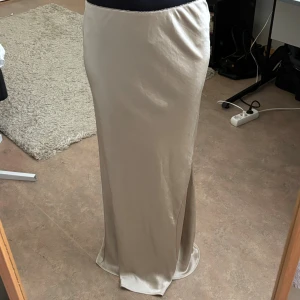 Beige satinkjol med slits - Supersnygg långkjol i beige satin-look med slits på sidan. Kjolen har en figurnära passform och skimrande yta som ger en lyxig känsla. Perfekt för dig som gillar stilrena och eleganta plagg med lite edge. Har sömm som har lossnat som man kan se på bild 3 o 4