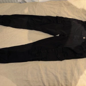 Svarta cargopants från Jack & Jones - Svarta cargopants från Jack & Jones med tapered fit och elastiska muddar vid bensluten. Byxorna har flera praktiska fickor på sidorna och är tillverkade i bomull. Perfekta för en avslappnad och streetig stil. 