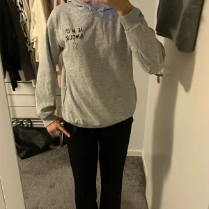 Grå hoodie från Gina Tricot med tryck - Grå hoodie från Gina Tricot Young med svart texttryck 'Je m'en amour' och en stjärna på både fram- och baksidan. Mjuk insida, huva med snörning och långa ärmar. Väldigt bra skicka och ass snygg💕