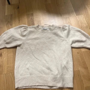 Beige stickad tröja med puffärm från ONLY - Säljer en beige stickad tröja från ONLY med puffade axlar och rund hals. Tröjan har ribbade muddar vid ärmslut och nederkant, vilket ger en snygg och modern look. Perfekt för dig som gillar stilrena och trendiga plagg.