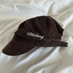 Brun manchesterkeps från Billabong - Säljer en brun keps från Billabong i mjuk manchester med böjd skärm och justerbart spänne bak. Kepsen har broderad logga framtill i vitt och en cool vintagekänsla. 