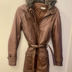 Brun skinnparkas med fuskpäls från Goldstein. Vintageinspirerad! - läderjacka för kvinnor i en snygg brun färg. 2-i-1 modell med avtagbar innerdel som gör den perfekt både för höst och vinter. Klassisk design, hållbar kvalitet och i mycket fint skick.  