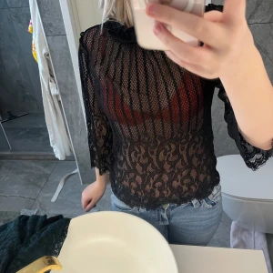 Svart spetsblus med trekvartsärm - Säljer en svart transparent spetsblus med snyggt mönster och trekvartsärmar. Blusen har både ränder och blommiga detaljer i spetsen, perfekt för dig som vill sticka ut lite extra. Snygg att styla med jeans eller kjol!
