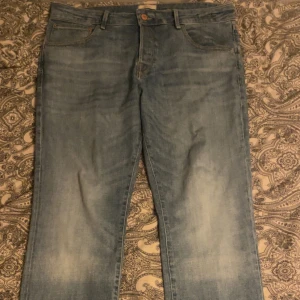 Ljusblå jeans från Jack and Jones - Säljer ett par ljusblå jeans från Jack & Jones med klassisk femficksdesign och snygga slitningar framtill. Jeansen har raka ben och normal passform, tillverkade i mjukt bomullsjeans. Bakfickorna har Jack & Jones signatursöm och läderpatch i midjan.