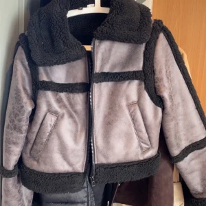 Grå bikerjacka med svarta detaljer - Säljer en grå biker jacka  i storlek S med svarta, fluffiga detaljer och dragkedja framtill. Jackan har två snedställda fickor och en bred krage som ger en cool look. Perfekt för dig som vill ha en varm och trendig jacka till höst och vinter.