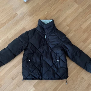 Vändbar pufferjacka svart och ljusblå - Säljer en vändbar pufferjacka med ena sidan svart och andra sidan ljusblå. Jackan har hög krage, dragkedja, två fickor med knappstängning och dragsko nertill. Perfekt för dig som vill variera din stil och hålla dig varm under kalla dagar.