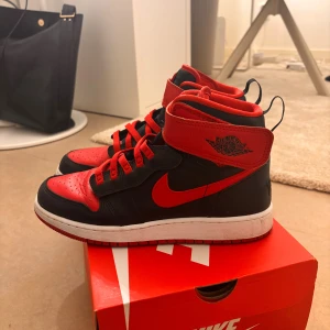 Nike Air Jordan 1 High röd/svart - Säljer ett par Nike Air Jordan 1 High i klassisk röd och svart färg. Skorna har högt skaft, röd swoosh och snörning, samt den ikoniska Air Jordan-loggan på sidan. Ovandelen är i skinn och sulan är vit med röd undersida. Perfekta för dig som vill sticka ut med en tidlös sneaker.