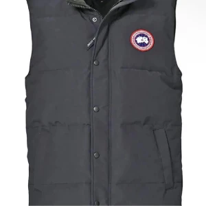 Mörkgrå dunväst från Canada Goose XS - Snygg mörkgrå dunväst från Canada Goose med klassisk logga på bröstet. Västen har hög krage, tryckknappar och dragkedja framtill samt stora fickor med lock och en innerficka med dragkedja. Perfekt för kalla dagar och riktigt stilren look.