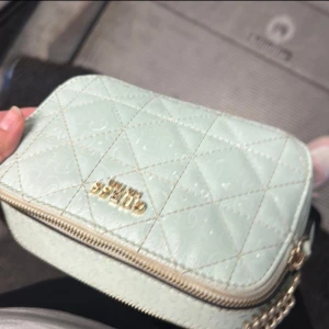 Ljusgrön quiltad axelväska från Guess - Säljer en ljusgrön quiltad axelväska från Guess med guldfärgade detaljer och kedjerem. Väskan har dragkedja och diskret logomönster i materialet. Perfekt storlek för det viktigaste och riktigt snygg att bära crossbody.