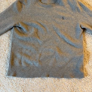 Grå kashmirtröja från Polo Ralph Lauren - Säljer en stilren grå kashmirtröja från Polo Ralph Lauren. Tröjan har rund halsringning, långa ärmar och diskret broderad logga på bröstet. Ribbstickade muddar vid ärmslut och nederkant ger en snygg finish. Perfekt för dig som gillar klassisk och enkel stil. Original pris var 1500 men säljer den för 450kr Priset är dock förhandlingsbart😊