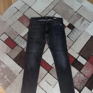 Replay Anbass svarta jeans - Säljer ett par svarta Replay Anbass jeans med snygg tvätt och klassiska fem fickor. Jeansen har raka ben och diskreta detaljer på bakfickorna. Materialet är mjukt jeans och passformen är normal, perfekt för dig som gillar stilrena och bekväma jeans.