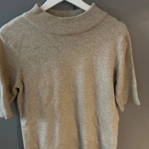 Beige stickad tröja med kort ärm - Beige stickad tröja med korta ärmar och bred ribbad krage. 