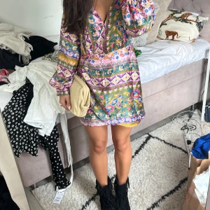 Färgglad kortklänning med blommigt mönster - Prislapp kvar!Superfin kortklänning i färgglada toner med blommigt och paisley-inspirerat mönster. Klänningen har v-ringning, långa puffärmar och en relaxed passform. Perfekt för dig 