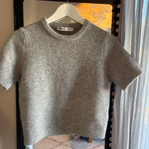 Grå stickad kortärmad tröja från Zara - Supermjuk grå stickad tröja från Zara med korta ärmar och rund halsringning. Ribbstickade detaljer vid ärmslut och nederkant ger en clean look. Passar till allt och är lätt att styla.