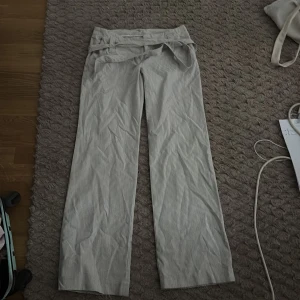 Randiga vida byxor med knytband - Snygga ljusgrå och vita randiga byxor med vida ben och knytband i midjan. Perfekta för en chill och trendig look. Byxorna har hög midja och är tillverkade i ett lätt material som passar bra till varmare dagar.