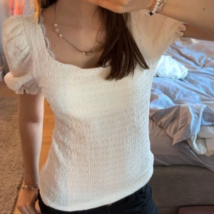 Vit puffärmad blus med spetskant - Supersöt vit blus med puffärmar och smockad struktur. Toppen har en fyrkantig ringning med fin spetskant och är tillverkad i ett lätt och luftigt material. Perfekt för vår och sommar när du vill känna dig extra söt och trendig. Accepterar dem flesta buden! Hör av er vid frågor!