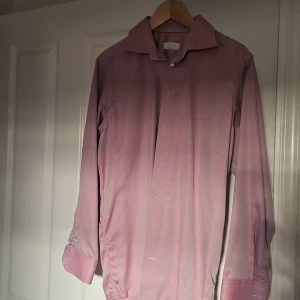 Rosa skjorta från Eton - Säljer en stilren rosa skjorta från Eton i klassisk modell med lång ärm och knappar hela vägen. Skjortan har en diskret randig struktur och är tillverkad i bomull. Perfekt för dig som vill ha en snygg och tidlös look.