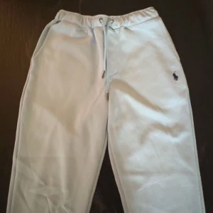 Ljusgrå mjukisbyxor från Polo Ralph Lauren - Snygga ljusgrå mjukisbyxor från Polo Ralph Lauren med klassisk broderad logga på benet. Byxorna har dragsko i midjan och är tillverkade i mjuk bomull. Perfekta för chill dagar eller när du vill vara bekväm men ändå se fräsch ut.