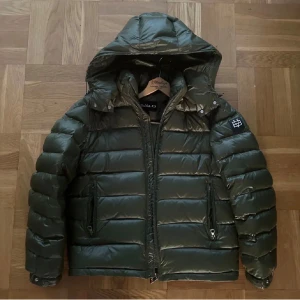 Snygg Olivgrön pufferjacka från Bvaldi - Säljer en riktigt snygg olivgrön pufferjacka från Bvaldi med huva och dragkedja. Jackan har quiltad design och lång ärm, samt en patch med Bvaldi-logga på ena ärmen. Denna jackan är perfekt och för att göra din outfit stilren samt skön och komfortabel som denna jackan är! 10/10 som ny använd endast 2 gånger!!! Köpt för 3000kr hos Bvaldi. Perfekt för kyliga dagar och även allmäna dagar där det är sol. Mega bra pris och väl värt pengarna ✅