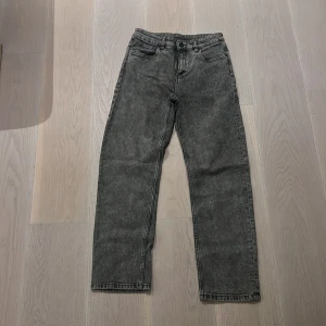 Grå tvättade raka jeans - Säljer ett par grå tvättade jeans med rak passform och klassisk femficksdesign. Jeansen har en normal midja och raka ben, perfekt för en avslappnad och stilren look. Materialet är robust denim som ger en snygg vintagekänsla.