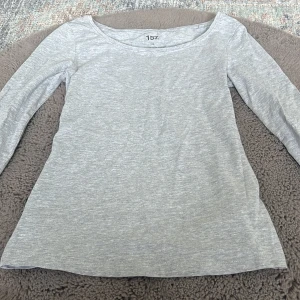 Ljusgrå långärmad tröja 157 XS - En basic ljusgrå långärmad tröja från 157 i storlek XS. Tröjan har rund halsringning och är tillverkad i en mjuk bomullsblandning med lite stretch för skön passform. Perfekt att styla med jeans eller kjol för en enkel och clean look. Tröjan har ett superduper litet hål på högra armen går säkert och fixa