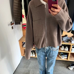 Brun cardigan jacka med dragkedja - Säljer en brun cardigan jacka från Åhlens med två stora fickor framtill och hel dragkedja. Jackan har en avslappnad passform, klassisk krage och är tillverkad i mjukt material. Perfekt för lager-på-lager och chill stil.