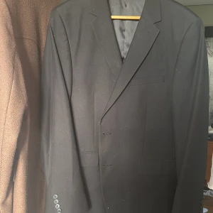 Svart kostym och kostymbyxor Dressmann slim fit 54 - Säljer en svart kostym från Dressmann i storlek 54, slim fit. Klassisk kavaj med snygg passform och matchande kostymbyxor. Fodrad insida med diskreta detaljer och flera fickor. Perfekt för dig som vill ha en stilren och enkel look.