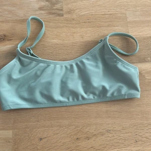 Ljusgrön bikiniöverdel för tonåring - Snygg ljusgrön bikiniöverdel med smala axelband och enkel spänne i ryggen. Modellen är sportig och stilren, perfekt för strand eller pool. Tillverkad i mjuk och stretchig polyesterblandning för skön passform.